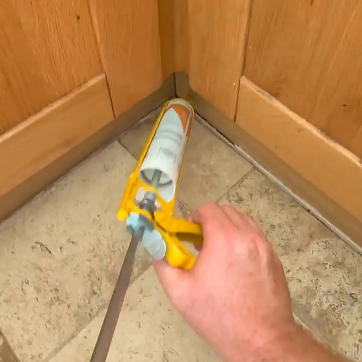 Clear silicone being run into the corner where oak kitchen plinths meet stone-effect floor tiles