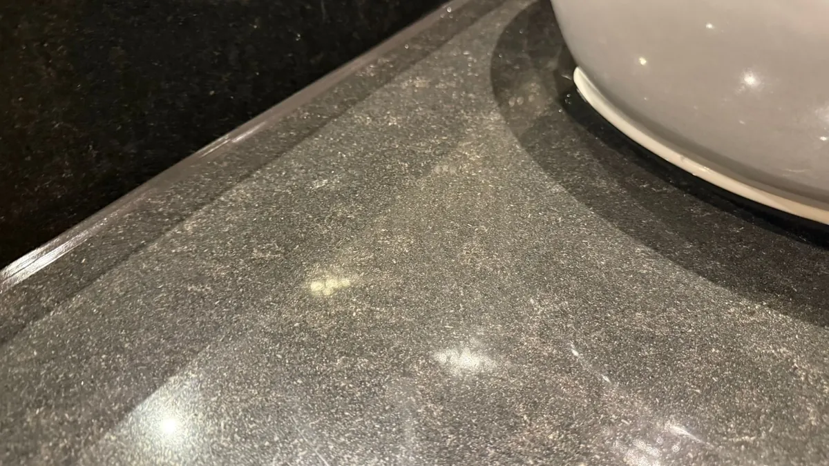 Smooth dark sealant bead where a speckled granite basin top meets its upstand, beside a grey basin