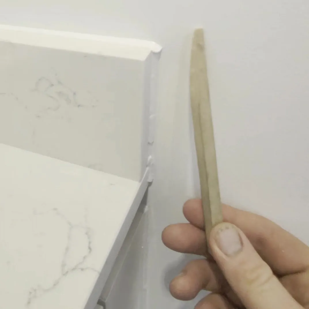 The finished sealant joint at the end of a white quartz upstand, with a wooden tooling stick held clear of the wall