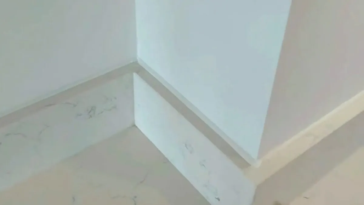 Finished white sealant joint where a white quartz floor upstand meets a white wall, running round an internal and an external corner