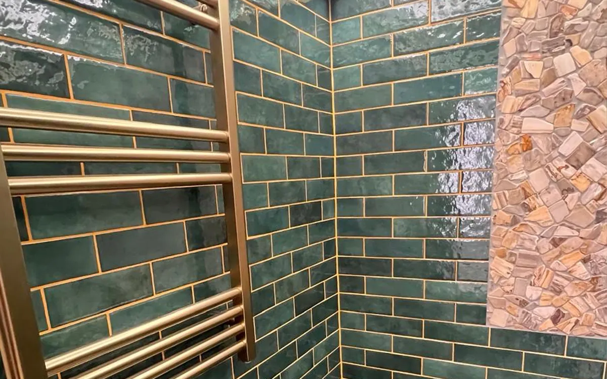Green gloss wall tiles meeting in a shower corner beside a brushed brass heated towel rail