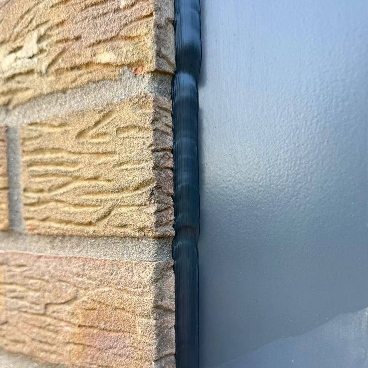 Lumpy, uneven old sealant between an anthracite window frame and buff brick