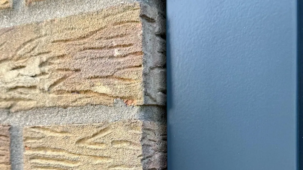 Neat, tight joint between an anthracite grey window frame and textured buff brick after a reseal