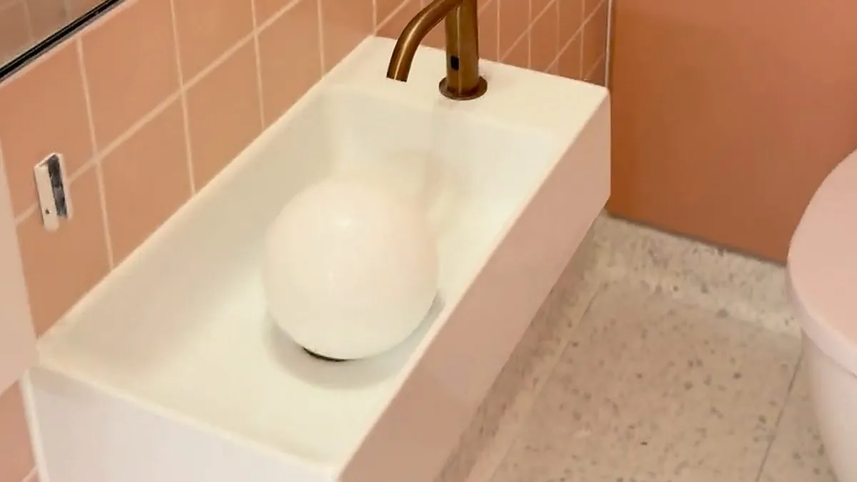 White wall-hung basin with a bronze sensor tap, freshly sealed against pink square wall tiles in a commercial washroom with a terrazzo floor