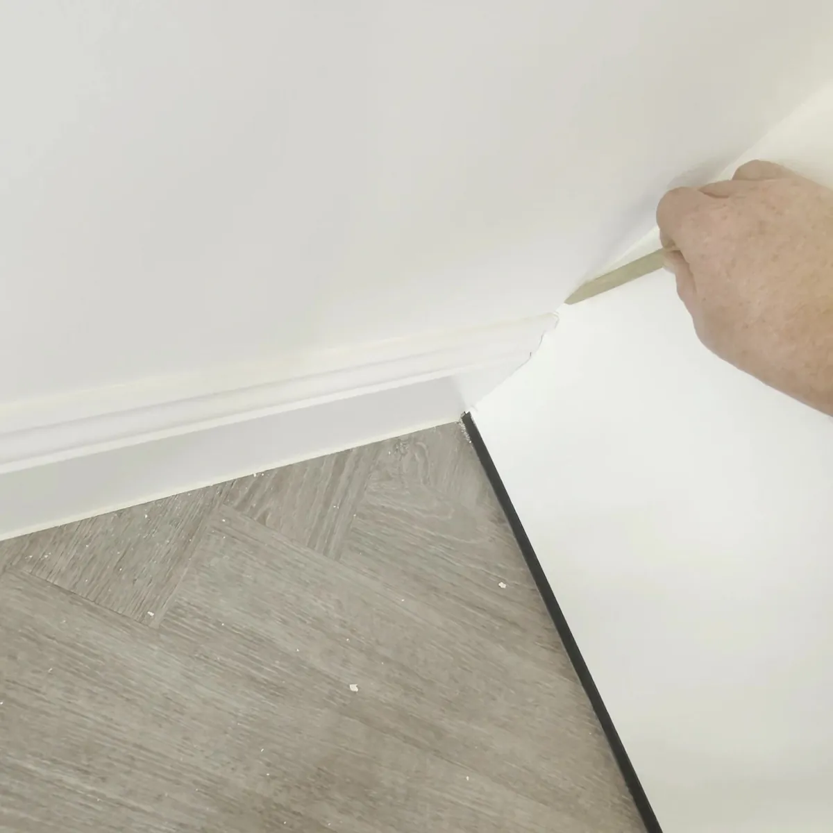 Wooden stick tooling a sealant joint where the end panel of a tall kitchen unit meets the wall and skirting above a herringbone floor