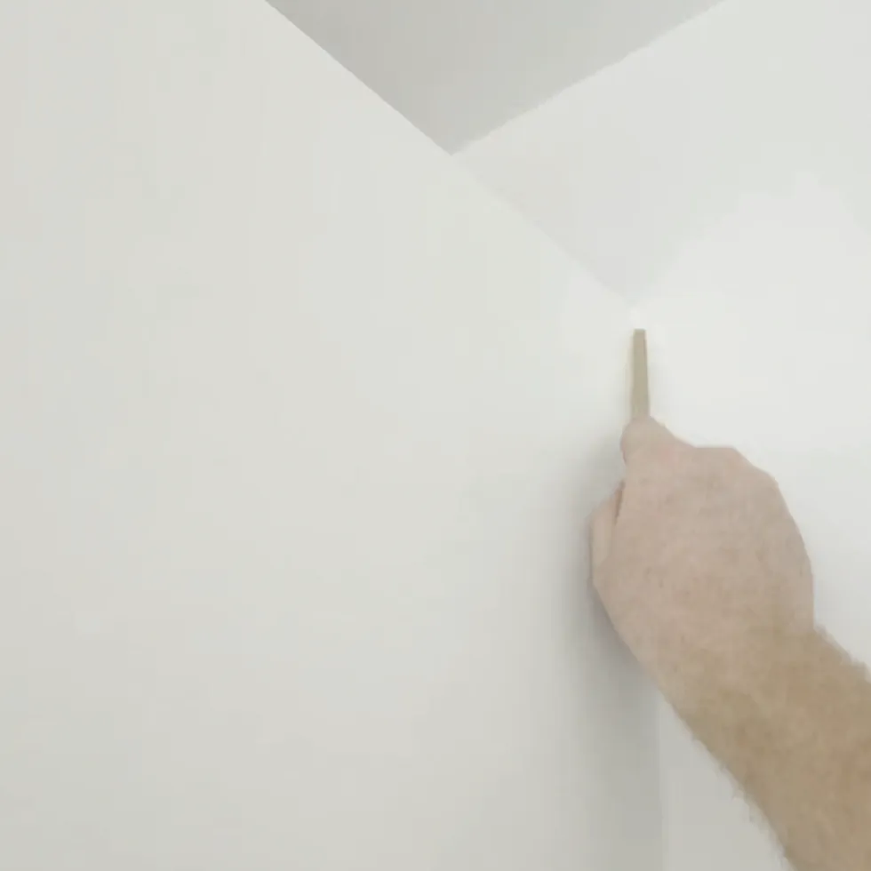Wooden tooling stick finishing a fresh sealant joint in a vertical internal corner between two white walls