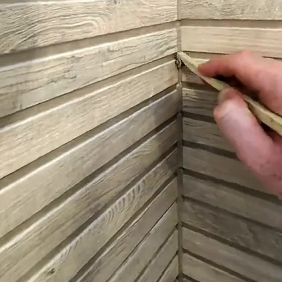 Hand tooling a fresh silicone joint into the corner of a shower lined with wood-effect ribbed tiles