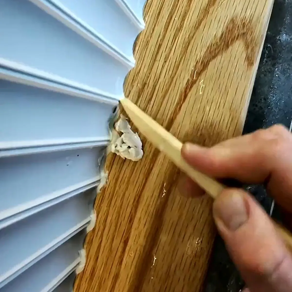 Sealant being tooled with a wooden spatula into the joint between curved white fluted wall panels and an oak trim